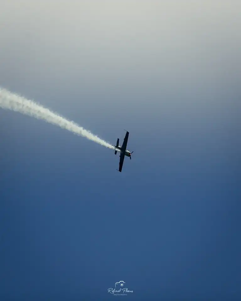 Aerobatic plane trailing smoke against a blue sky